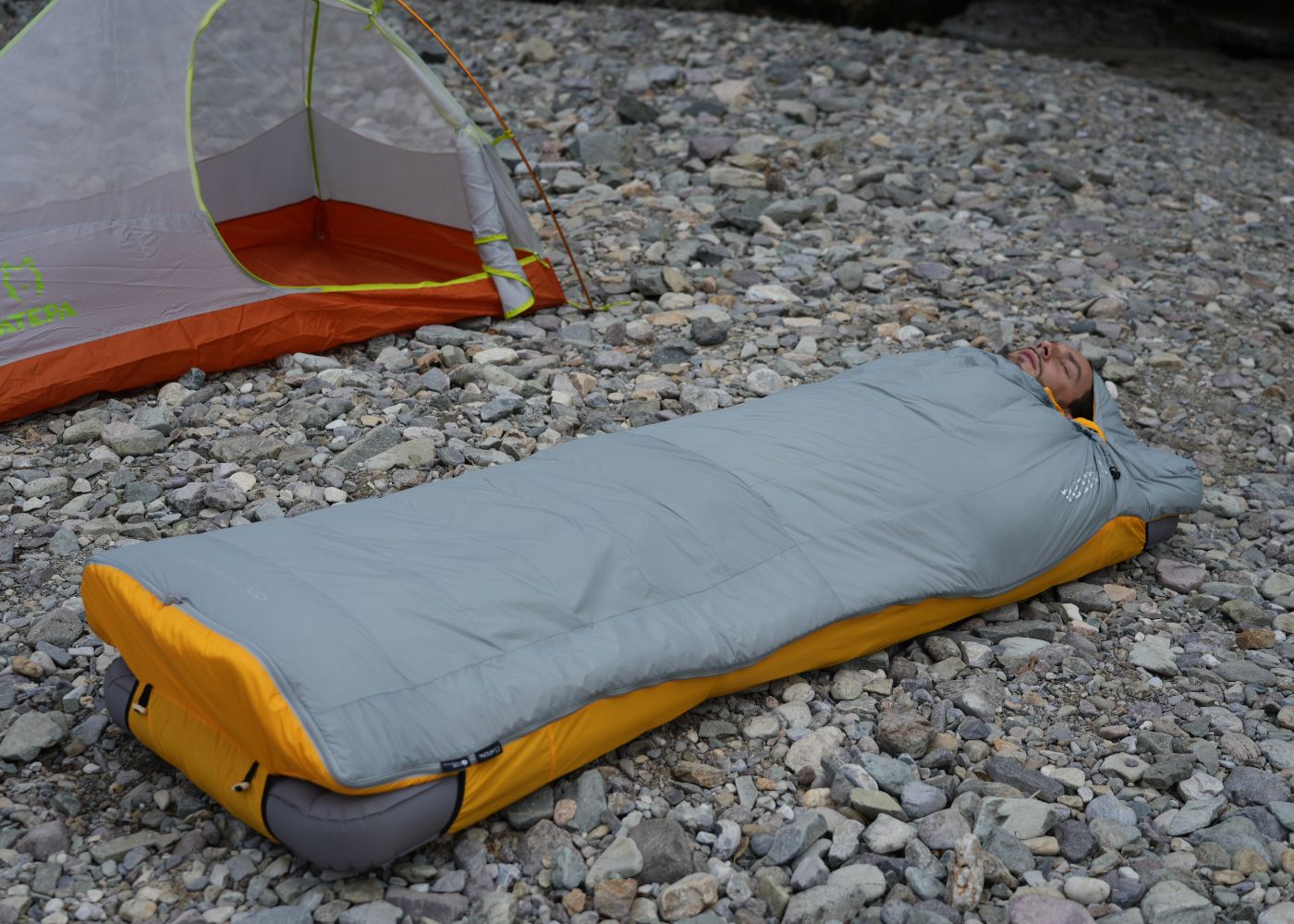 Down sleeping bag placed beside backpack for hiking, trekking, and camping adventures